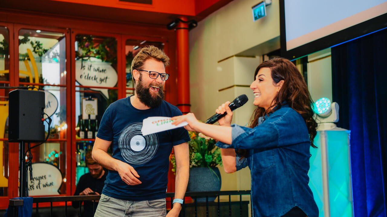 Raadsleden Bastiaan Bouwman en Melody Deldjou Fard presenteren met elkaar op het podium van een lokaal evenement.